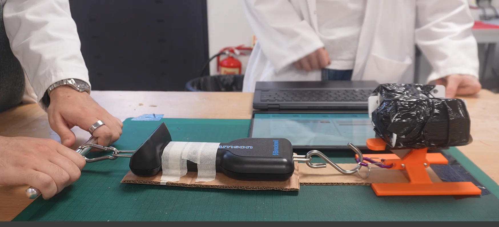 Drag force test: a force gauge pulling the weighted cutting head across cardboard on a cutting mat