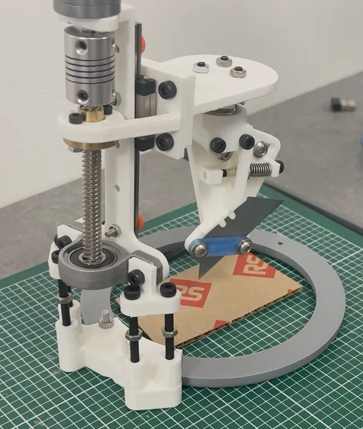 Cutting head prototype with lead screw, spring-loaded blade mount and cardboard on a cutting mat