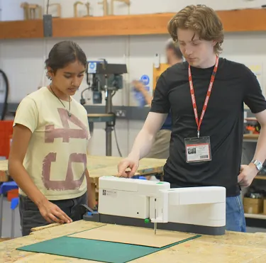 A student using the SwivelCut prototype on a workshop bench, guided by a team member
